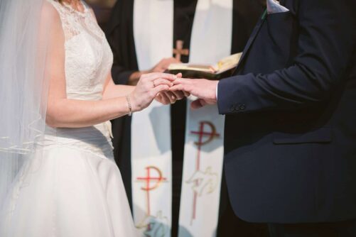 ślub kościelny - panna młoda zakłada obrączkę na palec pana młodego, w tle ksiądz